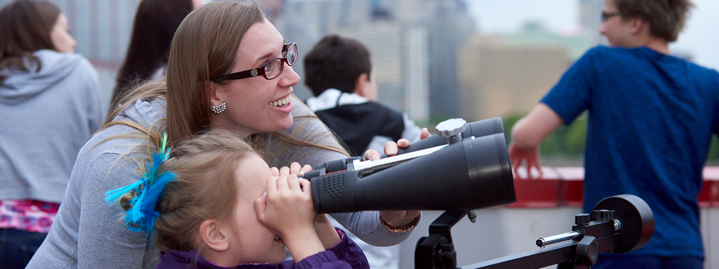 A woman helping a child look through a telescope