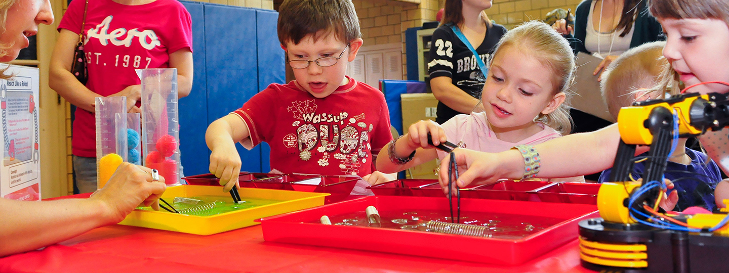 Young children use tweezers to explore objects in trays of water