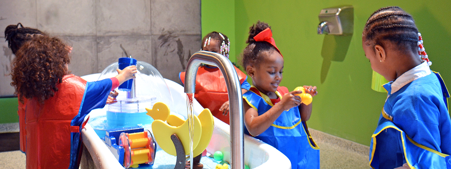 A group of preschool-aged girls play with the water exhibit in the Little Learner Clubhouse