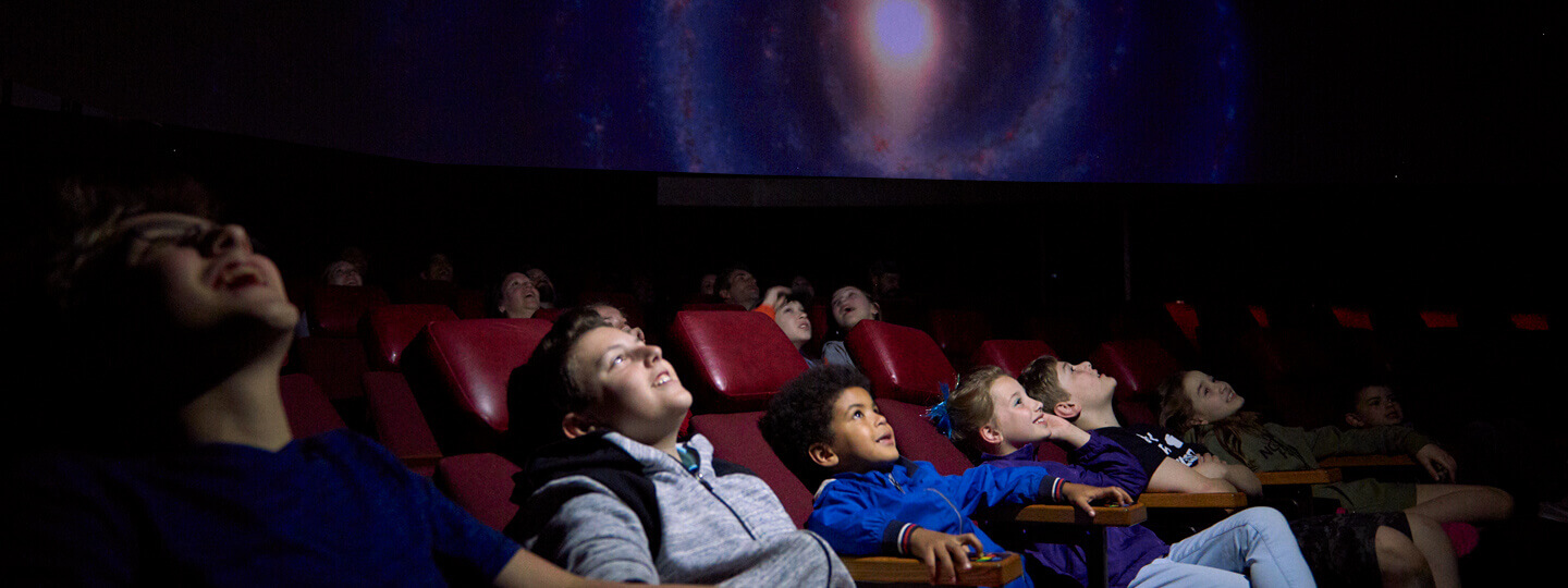 Children sitting in reclined seats smiling looking up at a screen