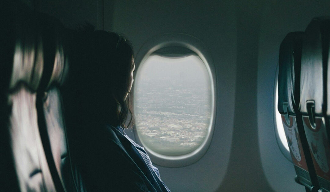 A woman seated on a plane, looking out the window