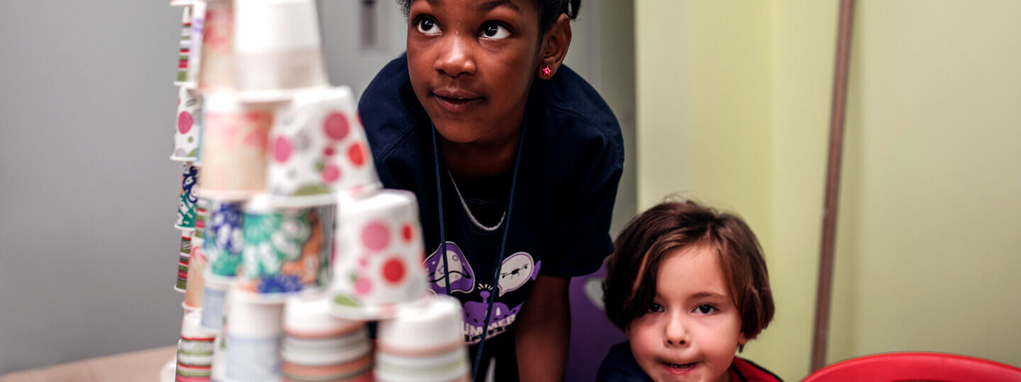 Two girls inspecting a tower made out of paper cups