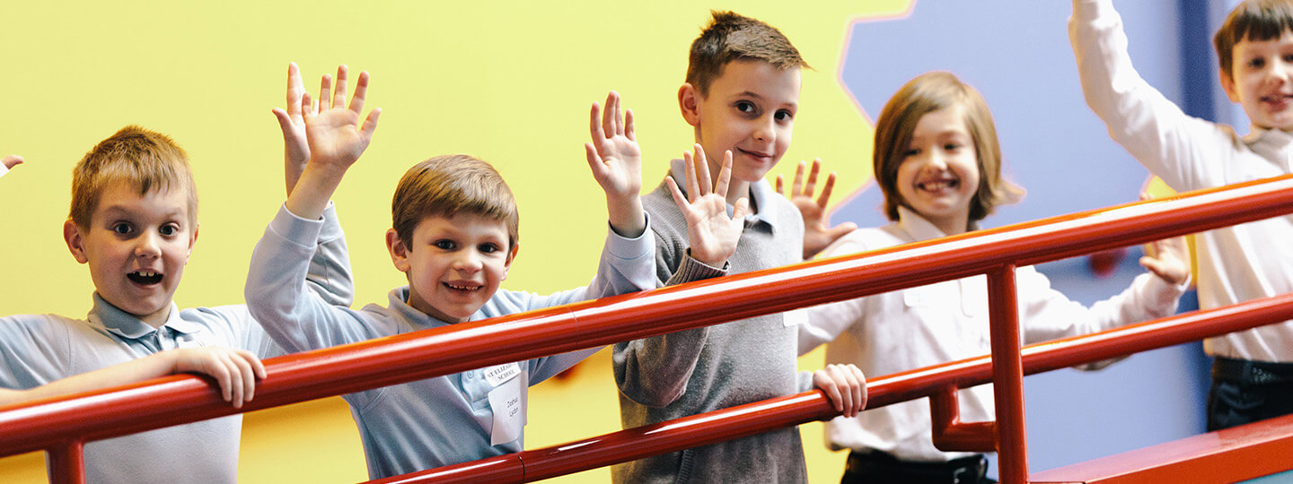 A group of students on a field trip wave excitedly at the camera as they travel between exhibits
