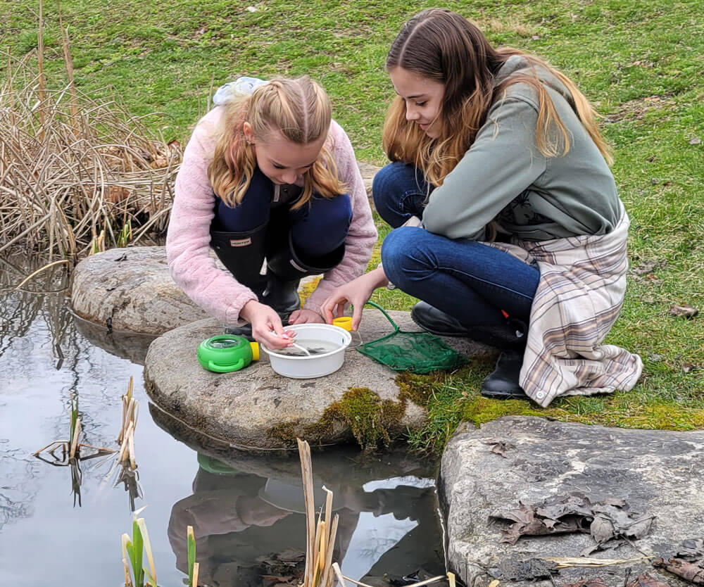Two girls taking water samples from a pond
