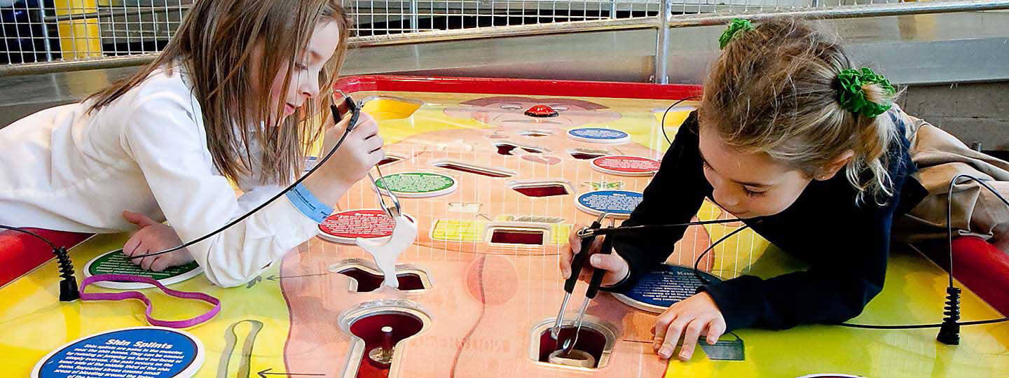 Young girls play with giant operation game interactive exhibit