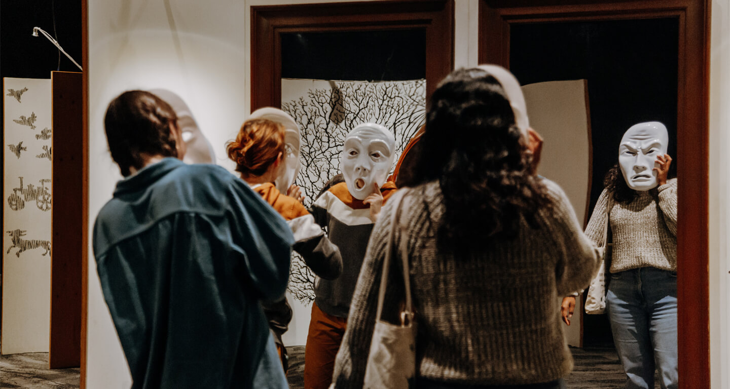 Three girls holding white masks with various expressions to their faces