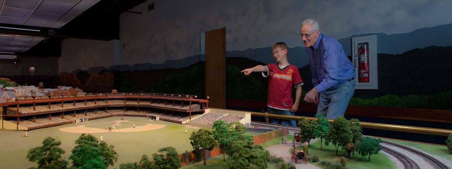 A man smiles as a child points to the replica baseball stadium in the Miniature Railroad and Village