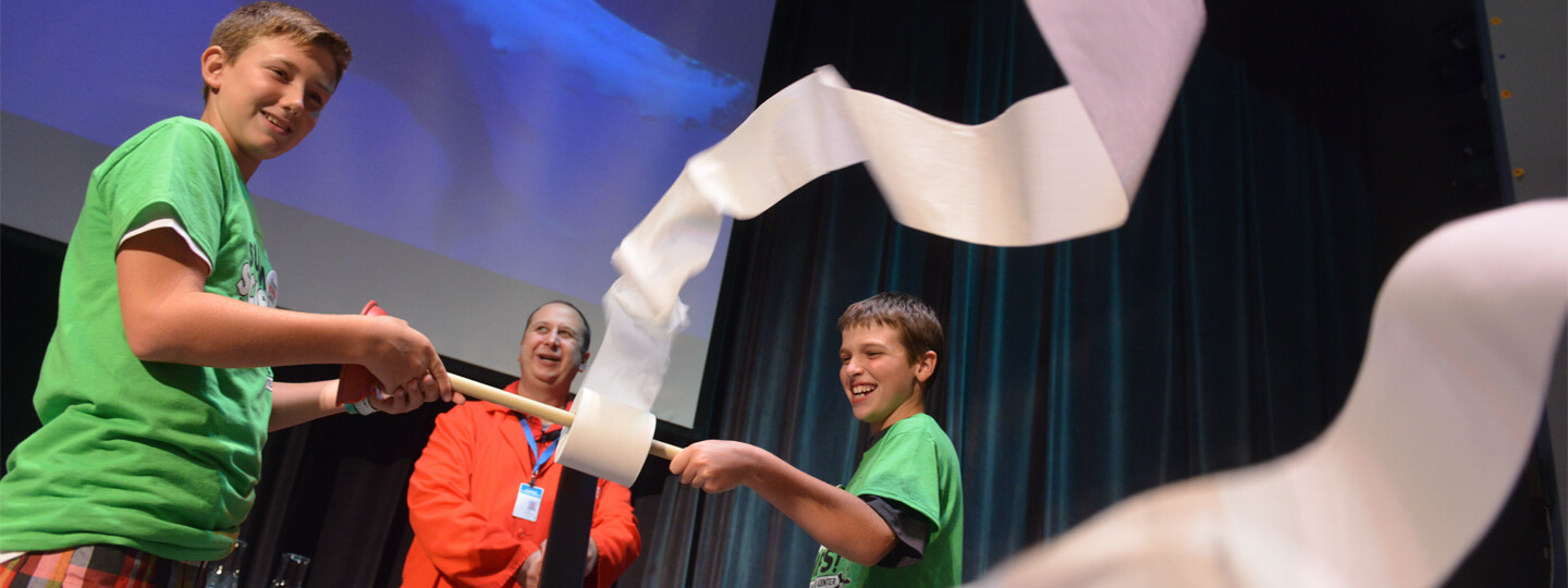 Two summer campers helping a Science Center volunteer on stage