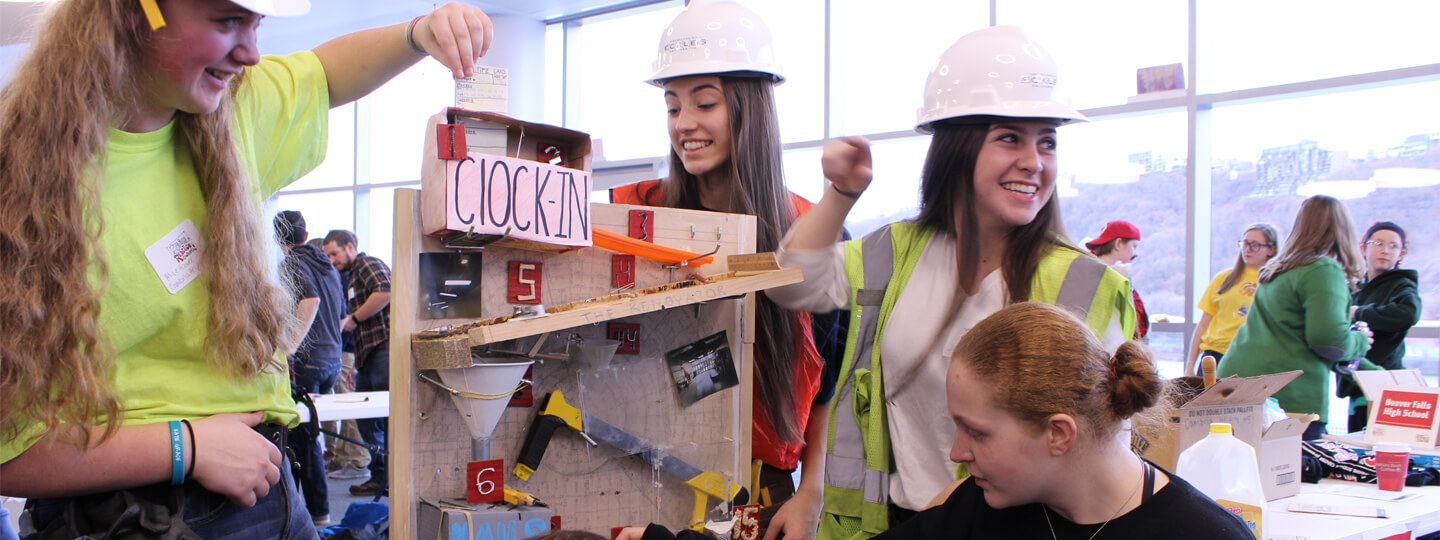 Girls wearing hard hats building a Rube Goldberg machine