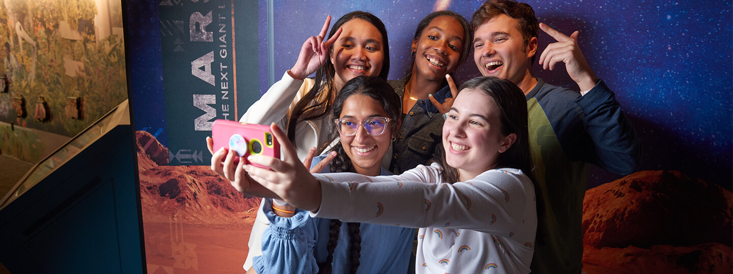 A group of teens taking a selfie in front of the Mars exhibit